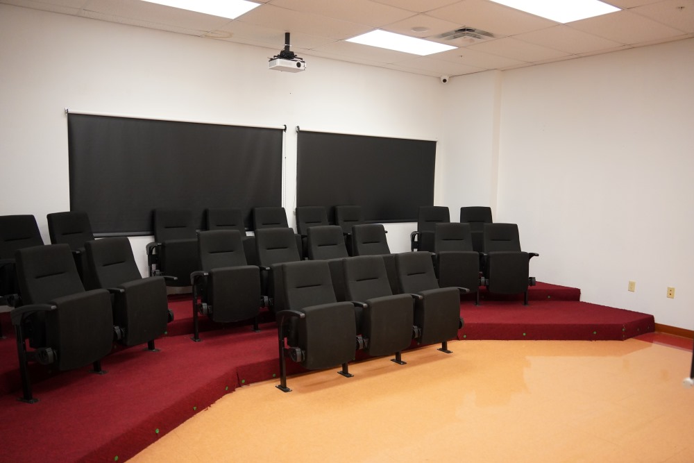 Small theater-style room with tiered rows of black seats